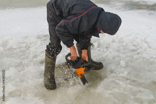 Man cutting chainsaw shell in ice