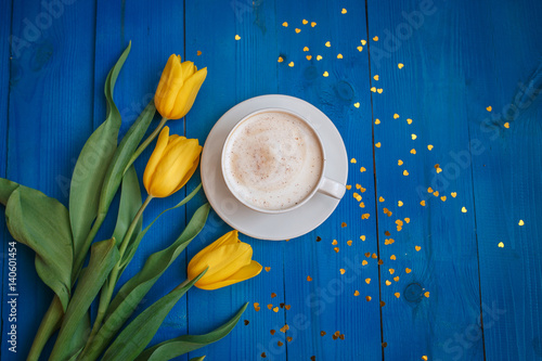 Coffee mug with yellow tulip flowers and notes good morning on blue rustic table from above, breakfast on Mothers day or Womens day .Spring  flowers bouquet photo