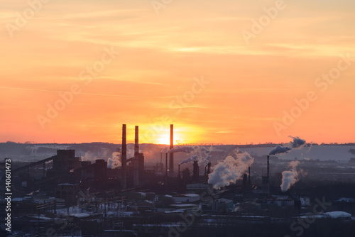 The pipes of the plant throw out toxic smoke at sunset. The sky is red. 