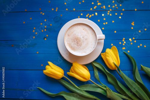 Coffee mug with yellow tulip flowers and notes good morning on blue rustic table from above, breakfast on Mothers day or Womens day .Spring  flowers bouquet photo