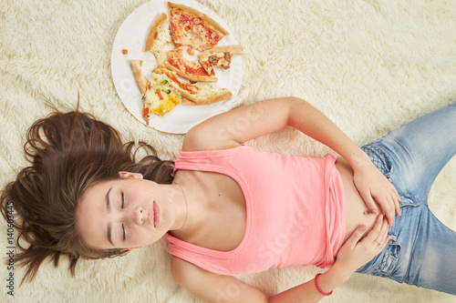 fun sad overeat girl lying with pizza pieces