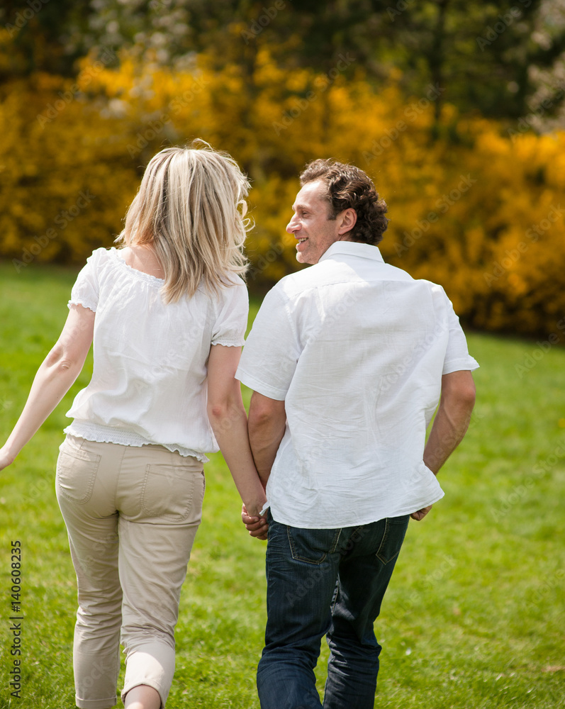 Couple holding hands with back to camera running through park Couple holding hands with back to camera running through park