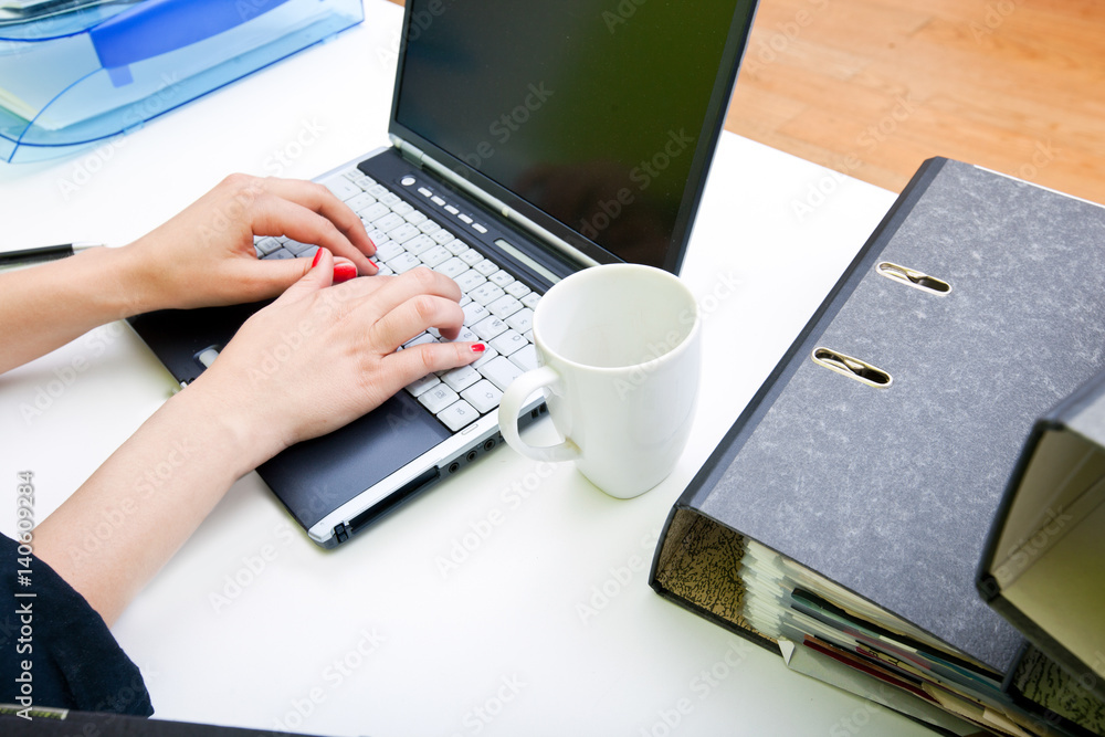 Close up of womans hands typing on laptop with folders and mug Close up of womans hands typing on laptop with folders and mug