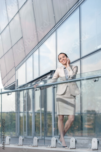 Full length of happy young businesswoman using cell phone at office balcony