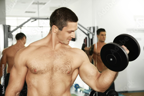 Young handsome man with dumbbell training in gym