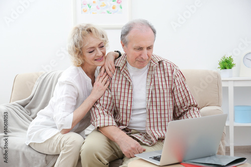 Happy senior couple using laptop at home