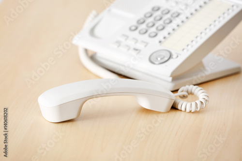 Telephone with picked up receiver on wooden table in office