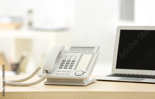 Telephone and laptop on wooden table in office