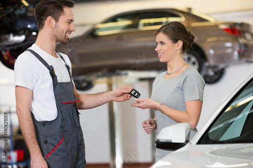 Happy repairman giving car key to woman in workshop © moodboard