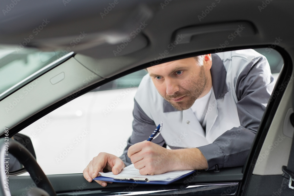 Male mechanic with clipboard checking car's interior in repair shop