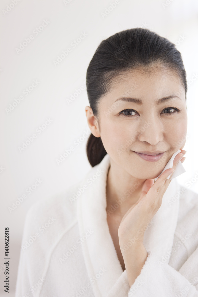 Woman in bathrobe putting lotion on face Woman in bathrobe putting lotion on face