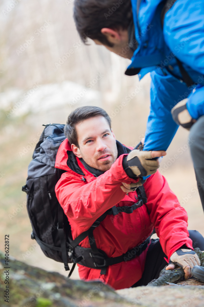 Fototapeta premium Male hiker helping friend while trekking in forest