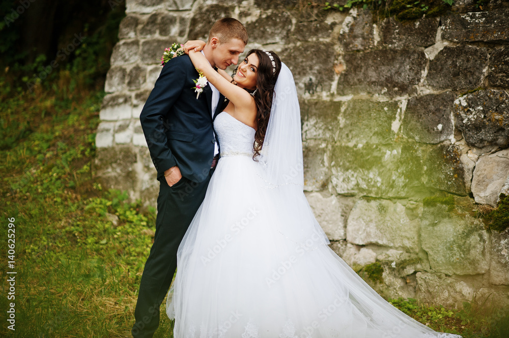 Young stylish wedding couple against old stone wall. Young stylish wedding couple against old stone wall.
