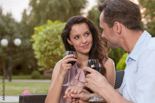 Romantic young couple holding hands while having red wine in park