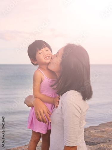 Happy family, mother and kid girl kissing with natural emotion smiling on sea background in the evening © zilvergolf
