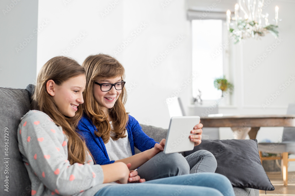 Happy sisters using digital tablet on sofa at home Happy sisters using digital tablet on sofa at home