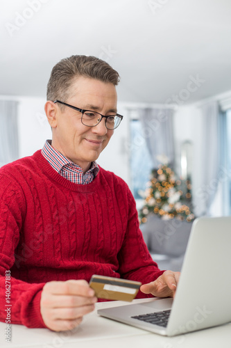 Smiling man using credit card and laptop to shop online at home during Christmas