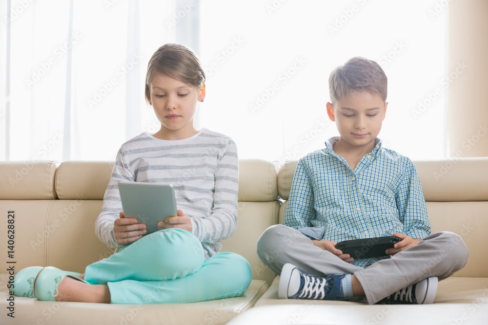 Cute siblings using technologies on sofa at home Cute siblings using technologies on sofa at home