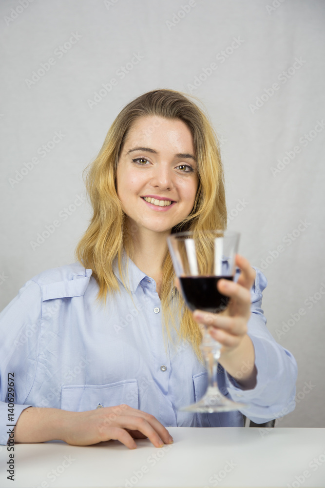 Young Caucasian white woman sitting at a table while drinking wine. She is blonde and pretty with light brown eyes. The background of the image is white. Young Caucasian white woman sitting at a table while drinking wine. She is blonde and pretty with light brown eyes. The background of the image is white.