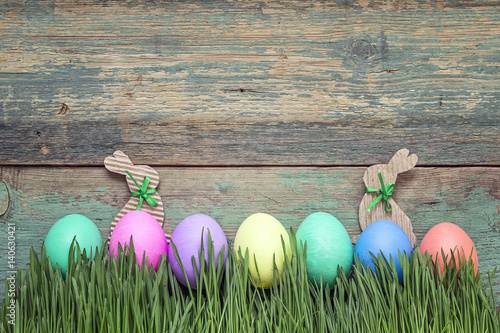 Easter eggs in fresh green grass on old wooden background.