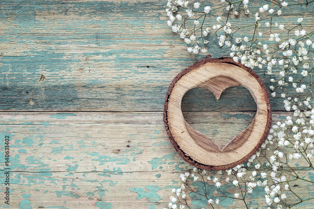 Small white flowers and heart carved in wood on the old grunge painted boards. Place for text. Small white flowers and heart carved in wood on the old grunge painted boards. Place for text.