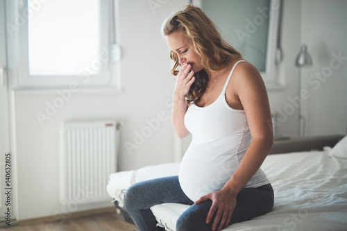 Beautiful pregnant woman lying in bed with cramps