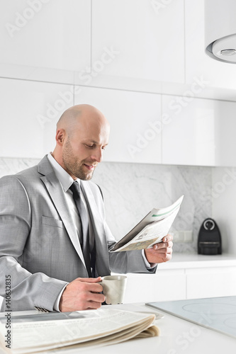 Mid adult businessman having coffee while reading newspaper in kitchen