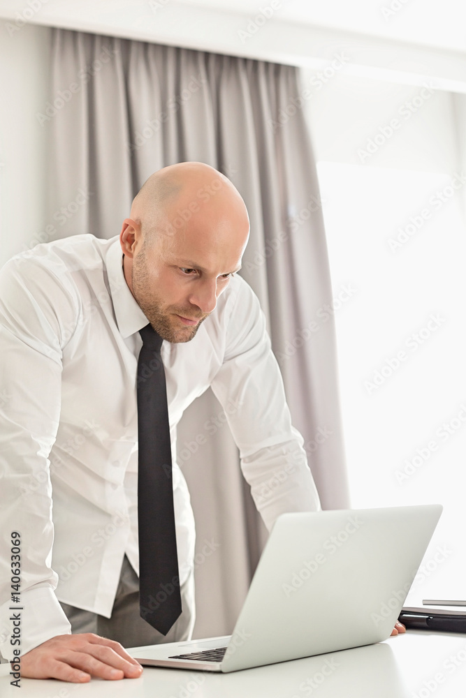 Mid adult businessman using laptop at table in home office Mid adult businessman using laptop at table in home office