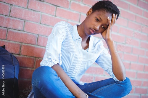 Sad schoolgirl sitting against brick wall