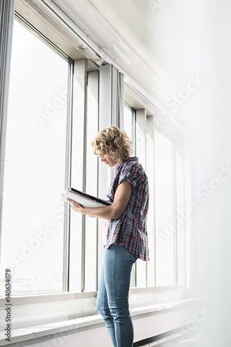 Side view of creative businesswoman reading file by window in office © moodboard