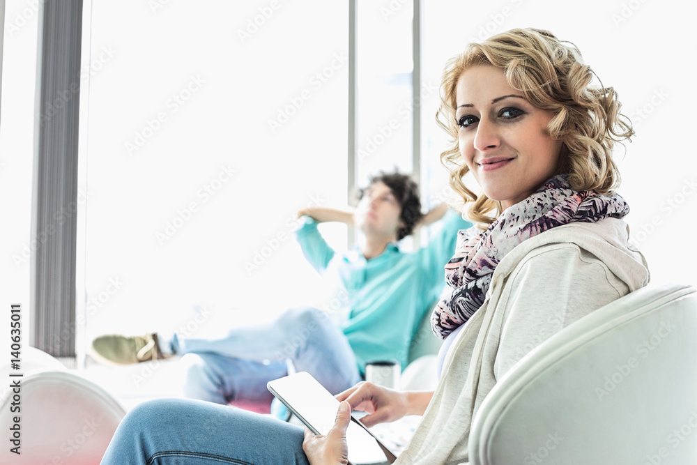 Obraz premium Portrait of creative businesswoman holding digital tablet at lobby with colleague relaxing in background