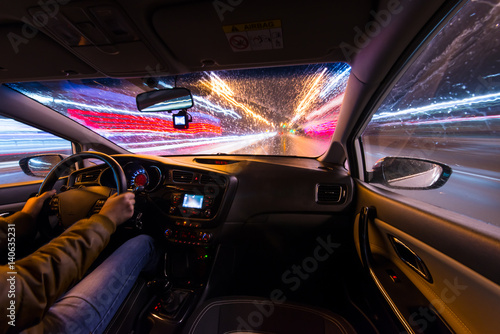 Night road view from inside car natural light street and other cars is motion blurred, during a rain