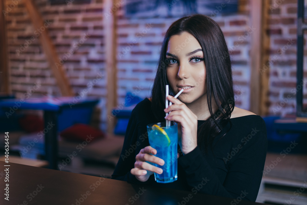 Beautiful attractive brunette young woman drinking blue lagoon cocktail in night club. Beautiful attractive brunette young woman drinking blue lagoon cocktail in night club.