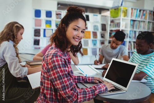 schoolgirl using laptop with her classmates 