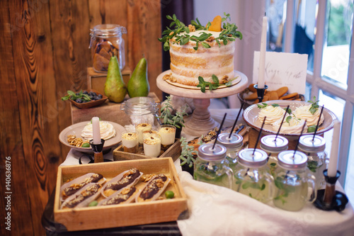 sweet bar with eclairs, lemonade,sweets and white cake  decorated with greenery in area of wedding party © tatyanasuyarova