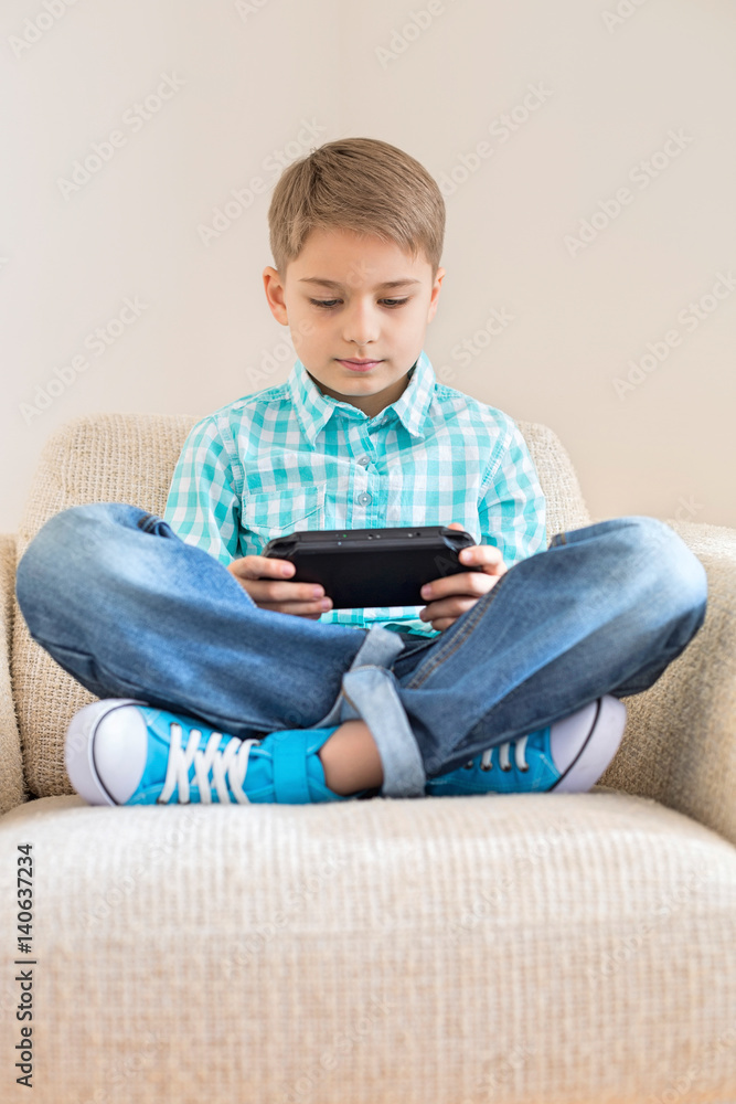 Boy playing hand-held video game on sofa at home Boy playing hand-held video game on sofa at home