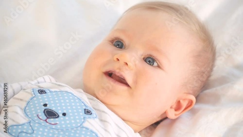 baby mit großen blauen augen und blonden haaren im bett