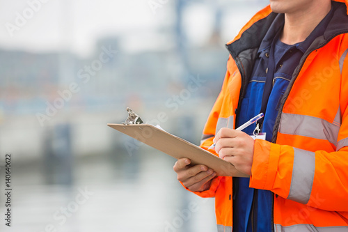 Foto Midsection of mid adult man writing on clipboard in shipping yard