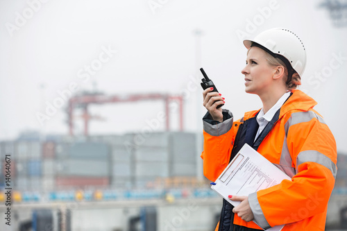 Canvas Print Side view of female engineer using walkie-talkie in shipping yard