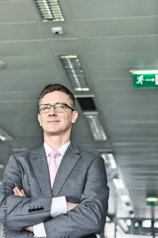 Middle-aged businessman standing with arms crossed in office Middle-aged businessman standing with arms crossed in office