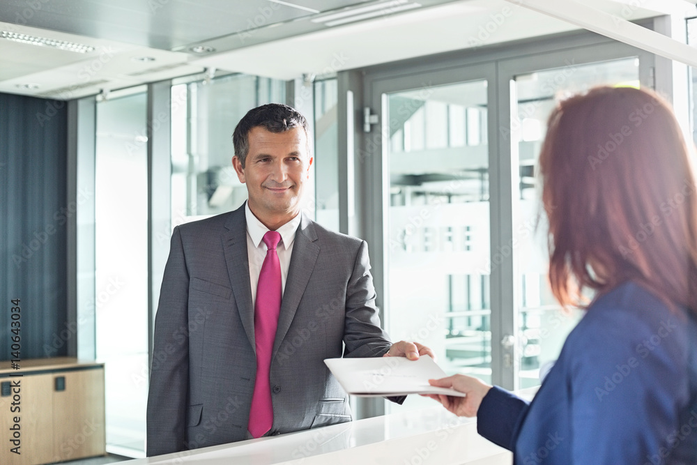 Businessman receiving document from receptionist in office Businessman receiving document from receptionist in office