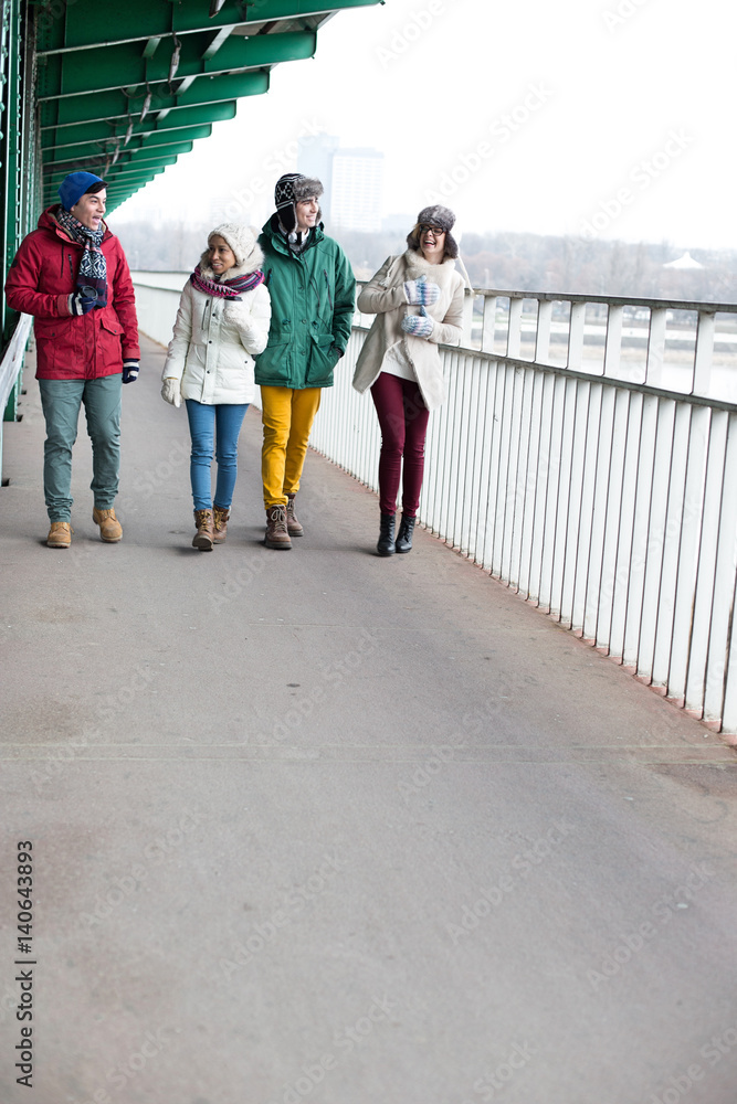 Multiethnic friends walking on footpath during winter Multiethnic friends walking on footpath during winter