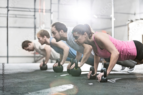 Side view of determined people doing pushups with kettlebells at crossfit gym