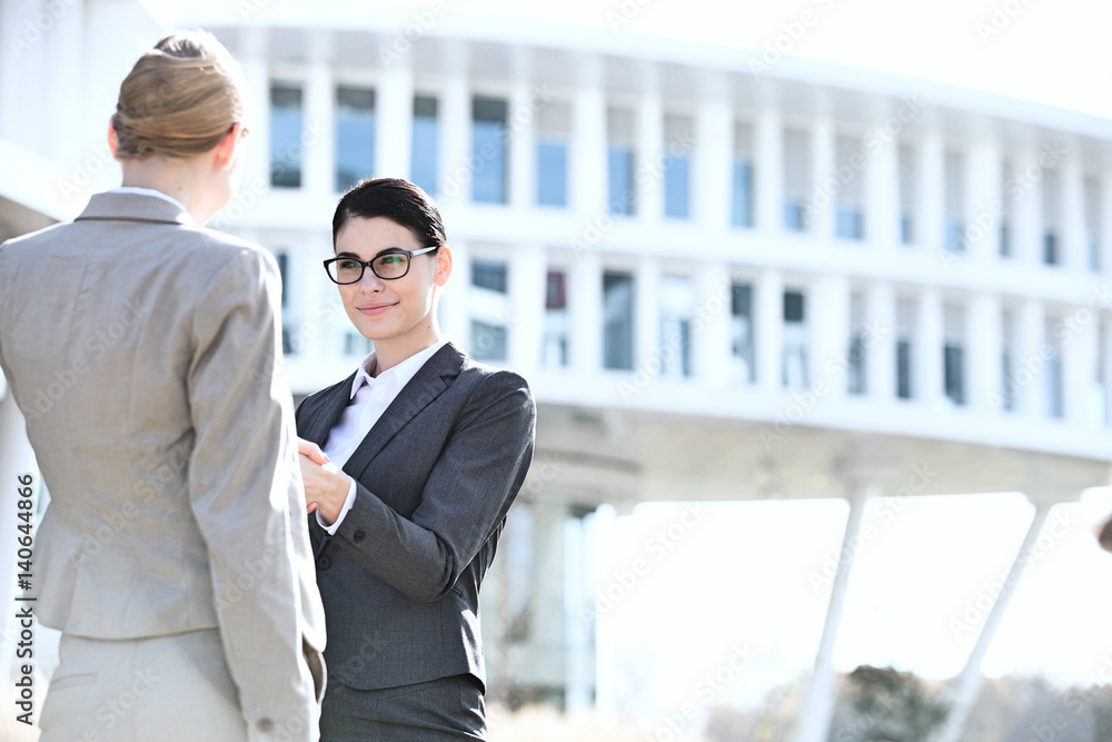 Businesswomen shaking hands outside office building Businesswomen shaking hands outside office building
