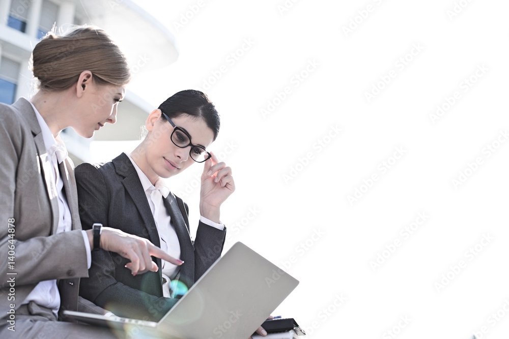 Low angle view of businesswomen using laptop against clear sky Low angle view of businesswomen using laptop against clear sky