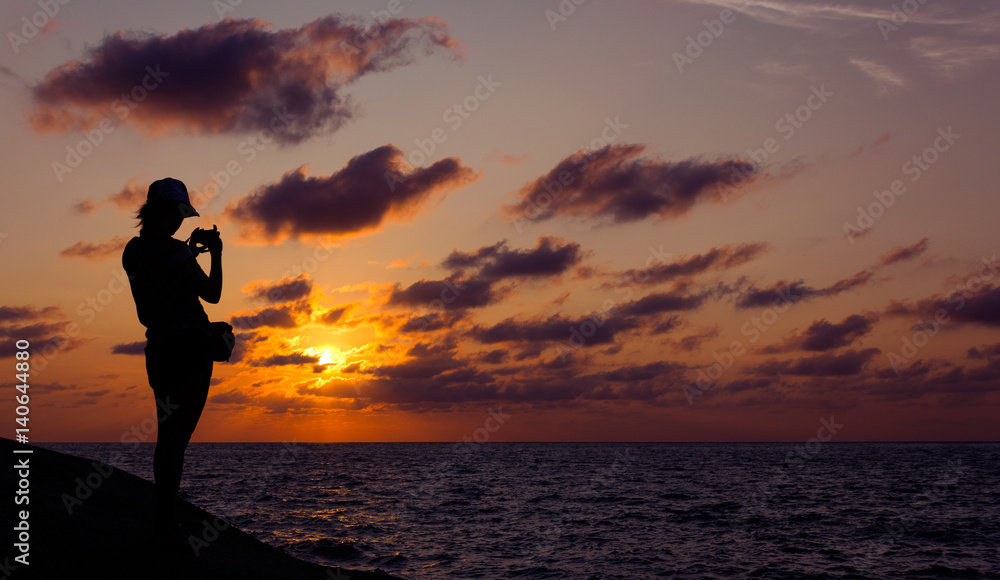 A person shooting the sunset. Back view of silhouette of person shooting the sunset to the smartphone. Horizontal outdoors shot.