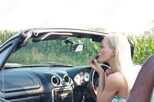 Rear view of woman applying lipstick in convertible