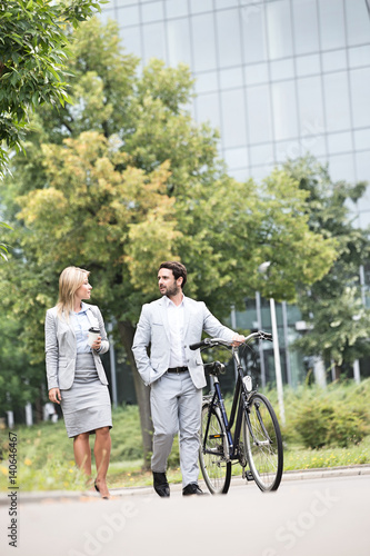 Businesspeople with bicycle conversing while walking on street