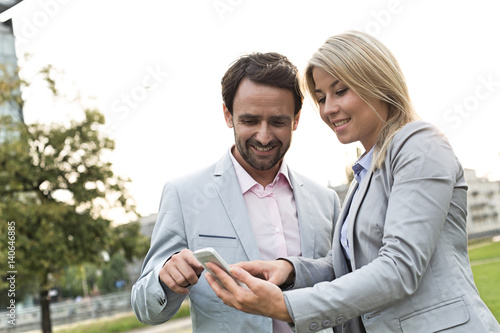 Happy business couple using smart phone at park