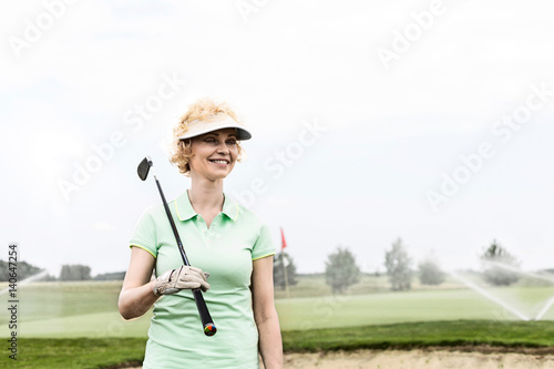 Happy middle-aged woman looking away while holding golf club